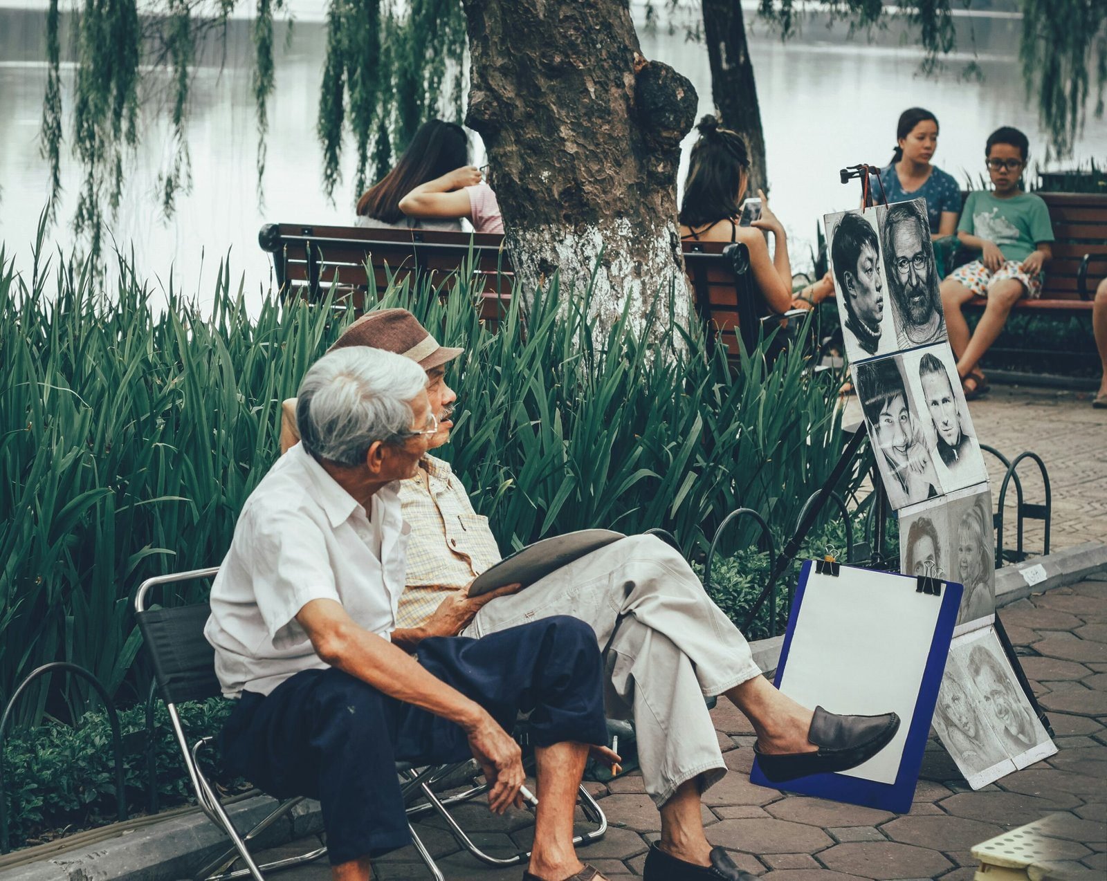 two men sitting on bench beside portrait paintings